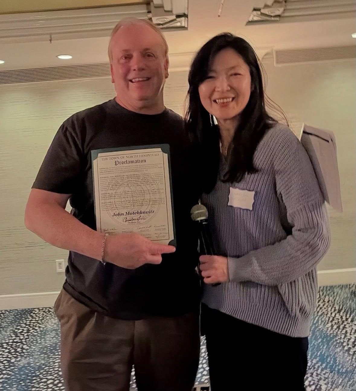 John Motchkavitz holding a proclamation with North Hempstead Councilwoman Christine Liu.